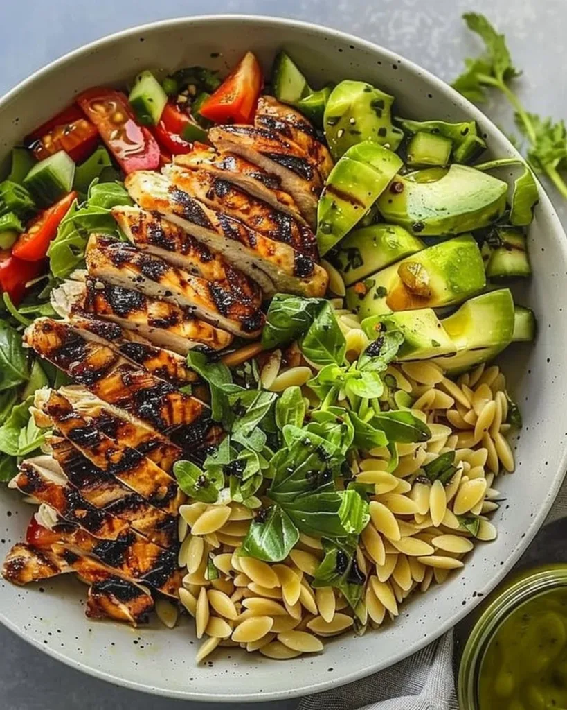 Grilled chicken salad with orzo, vegetables, and dressing in a bowl.