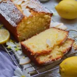 Sliced Coconut Lemon Loaf Cake on a wooden cutting board with a lemon wedge